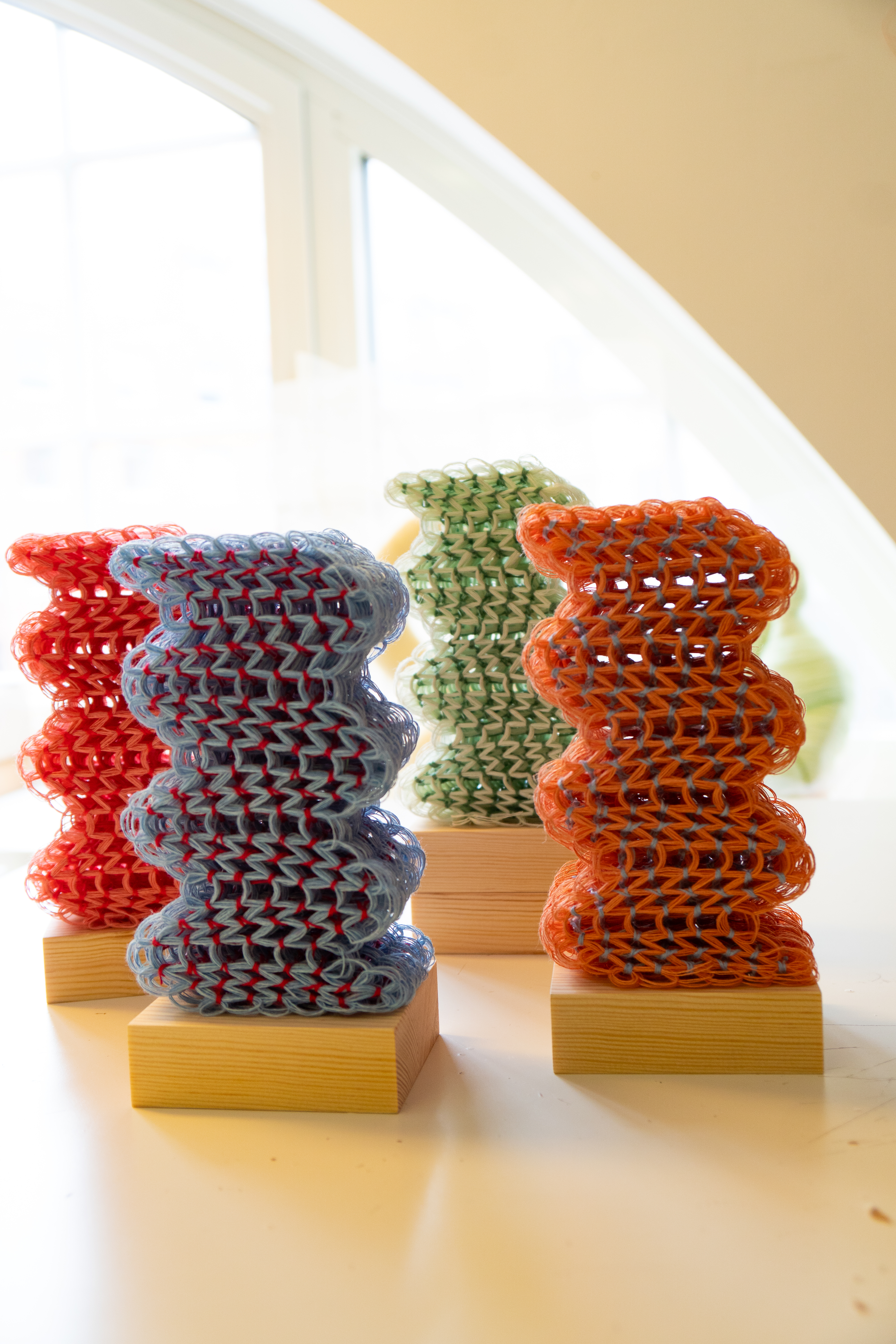 Fyra sprisskulpturer i garn och pärlor i färgerna blått, rött, grönt och orange
