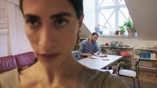 Kvinna tar selfie med man i bakgrunden